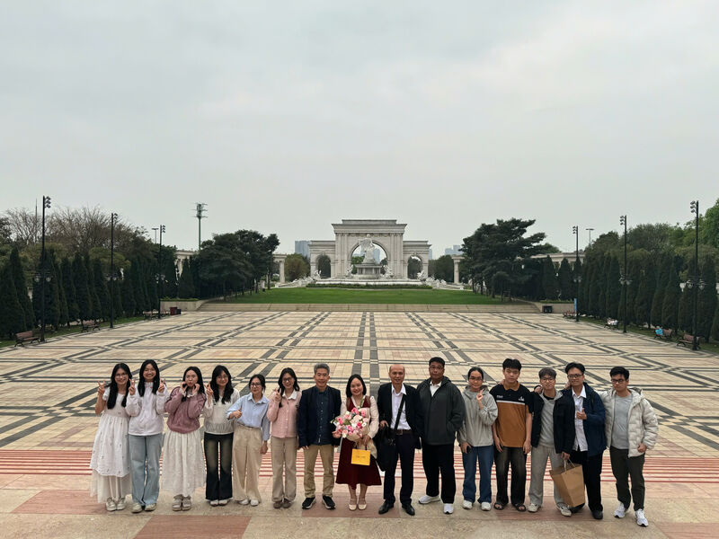 Sixteen members of the unit standing in a line across a wide paved plaza, with a colonnaded monument and fountain in the distance behind them.
